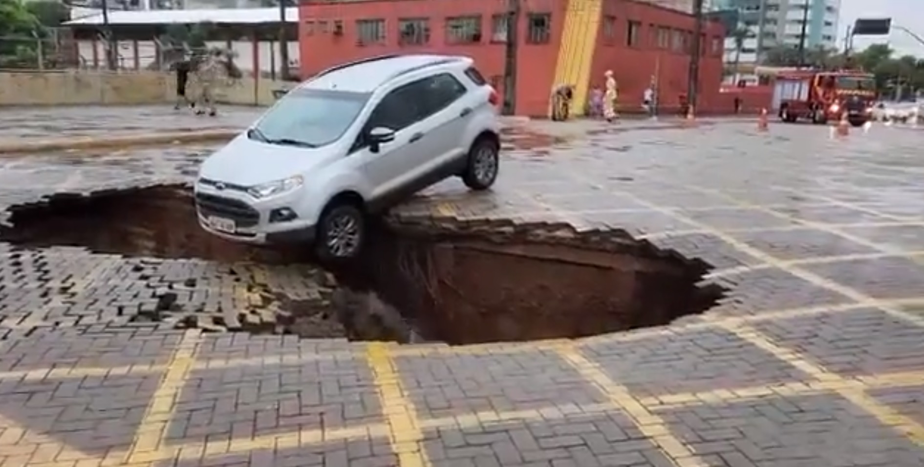 Asfalto cede em avenida e carro fica pendurado em cratera veja vídeo